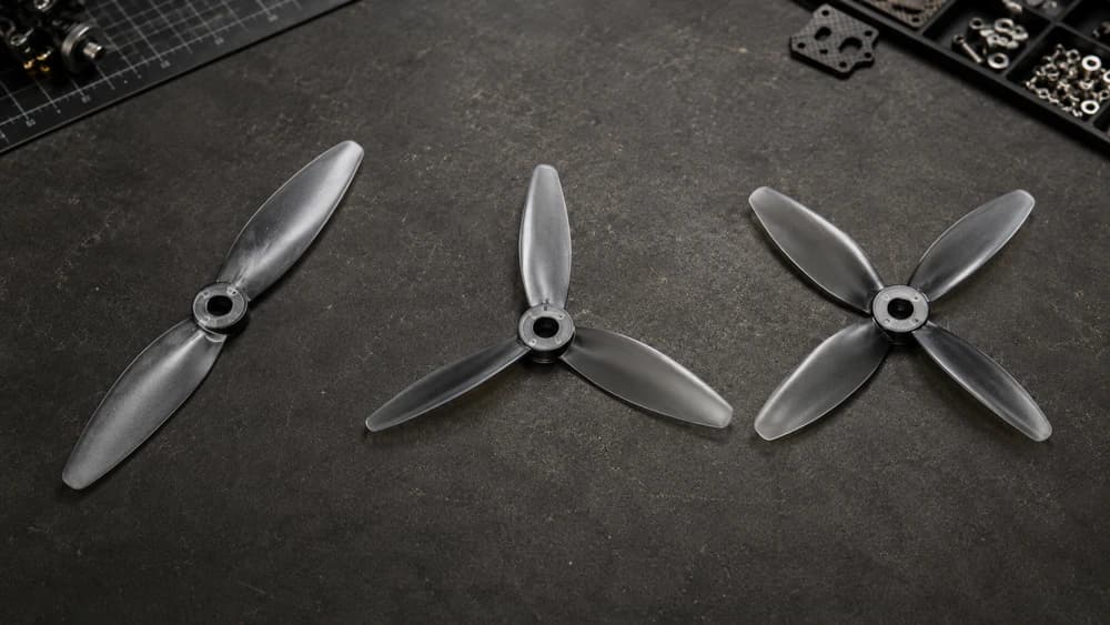 Side-by-side comparison of 2-blade, 3-blade, and 4-blade FPV propellers on a workbench